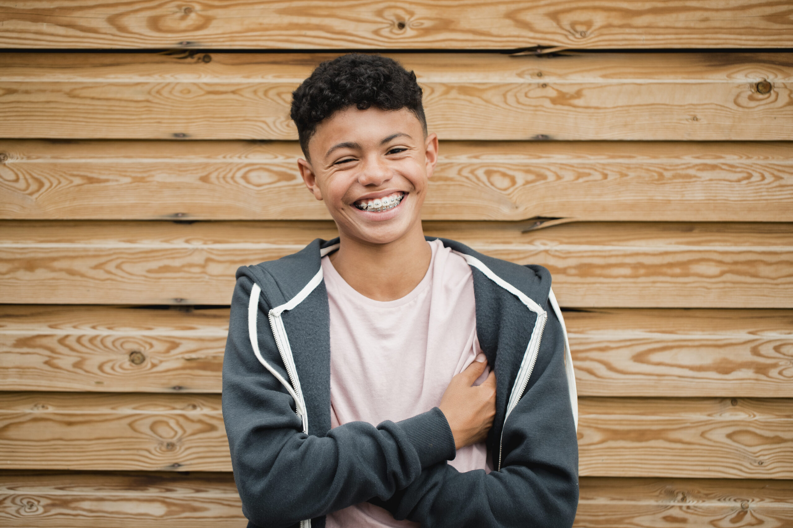 Headshot of a teenage boy standing, smiling and flowing his arms while looking at the camera.